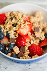 Healthy muesli breakfast bowl with granola made of toasted rolled whole-grain oats, organic honey, milk chocolate chips and graham cracker cookies served with fresh strawberries and huckleberries