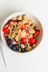 Müsli bowl with homemade granola made of toasted rolled oats, organic honey, chocolate chips and cookies served with fresh strawberries and blueberries on white table for healthy diet and nutrition