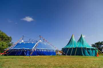 Two circus tents with colorful pennants at sunrise in a park