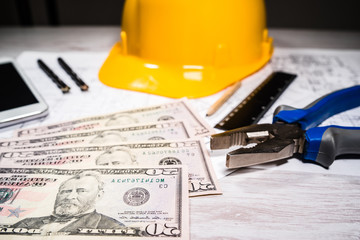 Construction industry costs money us dollars banknotes by tools safety equipment and blueprints