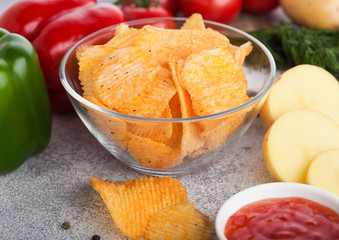 Glass bowl plate with potato crisps chips with paprika on light table background. Red and green paprika pepper with potatoes and sweet chilli sauce.