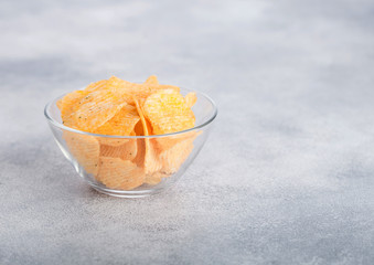 Glass bowl plate with potato crisps chips with paprika on light table background. Space for text