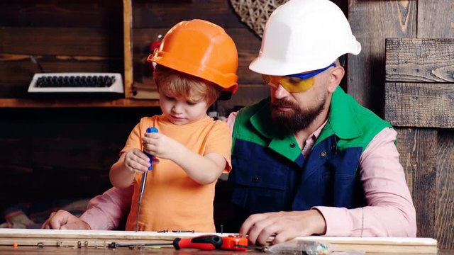 Boy busy in protective helmet learning to twist screws with screwdriver with dad. Workshop and handyman concept. Dad and son working with tools. Parent with busy son. Little boy using screwdriver.