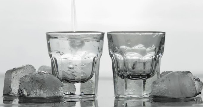 Pouring up two shot of vodka from a bottle into glass. White background