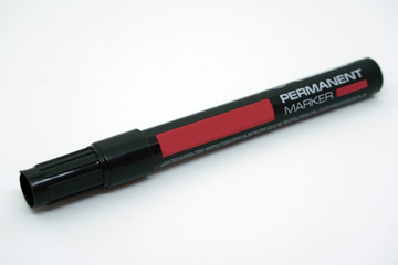 Closed permanent waterproof marker pen black color with red label close-up isolated on white background.