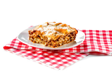 piece of lasagna with plate and checkered red napkin isolated on white background 