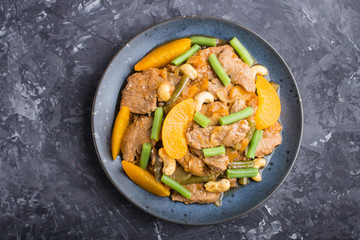 Fried pork with peaches, cashew and green beans on a black concrete background, close up.