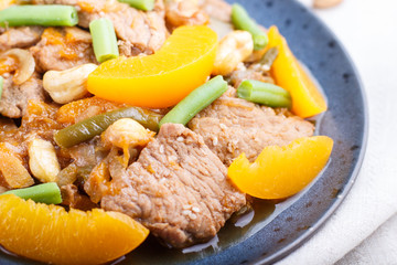 Fried pork with peaches, cashew and green beans on a black concrete background, close up, side view.