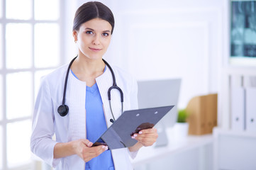 Young smiling female doctor with stethoscope holding a folder at doctor's office