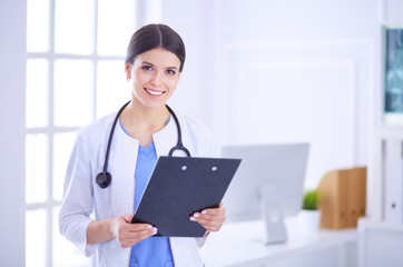 Young smiling female doctor with stethoscope holding a folder at a hospital's consulting room