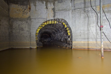 Flooded round underground drainage sewer tunnel with dirty sewage water flowing to collector