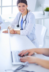 Smiling doctor using a laptop working with her colleagues in a bright hospital room