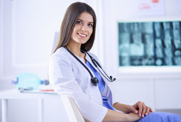 Beautiful female doctor sitting in a consulting room, smiling at the camera