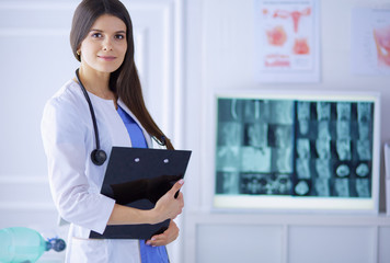 Beautiful doctor standing in a consulting room with a folder in her hands, thinking