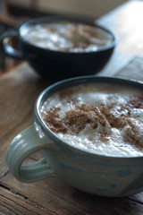 two big mugs of a hot foamy drink covered in whip cream and cinnamon