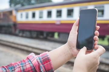 woman's hand holding and using smartphone, black screen with blur train background. subject is blur.