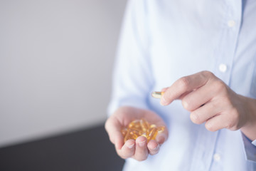 Healthy eating and diet nutrition concepts. vitamin and supplement. beautiful young woman holding yellow fish oil pill. female hand putting omega-3 capsule in mouth.