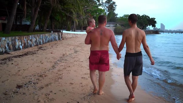 happy gay couple is resting on a beautiful tropical beach. LGBT concept. gay couple walking on the beach with a child