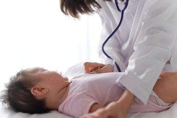 Obraz na płótnie Canvas Female doctor is listening heart pulse rate of cute newborn baby on the bed by using stethoscope in the room. Seen from side view of baby. Baby health care concept.