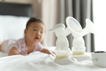 Breast milk in milk pump's bottles and pump machine on the bed with smiling baby crawling in background. The milk got from milk pump's machine and ready for the baby. Baby health care concept.