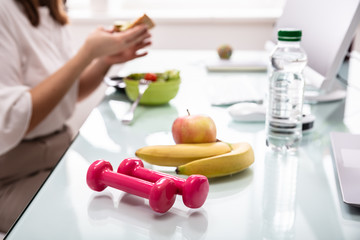 Water Bottle, Banana And Pink Dumbbells On Office Desk - Powered by Adobe