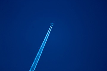 Two engine long-haul plane in the blue sky with contrail