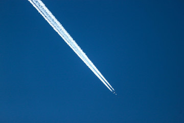 Jet airplane in the bright blue sky with huge contrail
