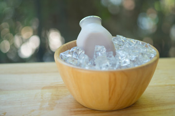 Fresh of strawberry milk plastic bottle on wooden bowl served with ice cubes
