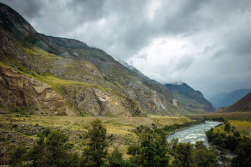 Atmospheric mountain landscape on a cloudy foggy day in the valley of Chulyshman. The river runs in a green valley between the rocks.