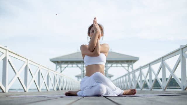 Young woman doing complex yoga exercise sitting in Garudasana arms exercise eagle pose. Amazing yoga landscape in beautiful sky and enjoying sea view on wooden floor