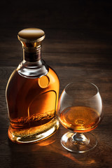 view of glass of  whiskey and a bottle aside on color wooden  background. 