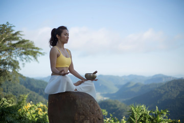 Young woman doing exercise yoga. sitting on the rock with tibetan singing bowl in the morning,Lotus...