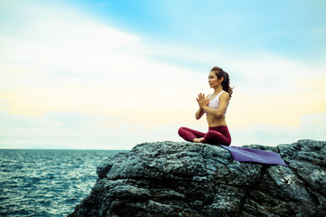 Young woman practicing yoga. sitting in doing meditation exercise, Namaste hands Pose, Amazing yoga landscape in beautiful sky and enjoying sea view, concept for exercising, health care