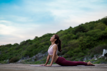 Fototapeta na wymiar Side view of woman doing exercise cobra pose (Bhujangasana) outdoors on a rock. Amazing yoga landscape view sky on evening sunlight nature evening outdoor, concept for exercising, health care