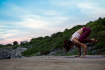 Young woman doing exercise yoga doing Crane (Crow) pose. Amazing yoga landscape in beautiful sky...