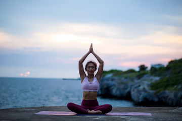 Fototapeta na wymiar Young woman doing exercise yoga. sitting in Sukhasana exercise, Easy Seat pose pose. Amazing yoga landscape in beautiful sky and enjoying sea view with evening, concept for exercising, health care