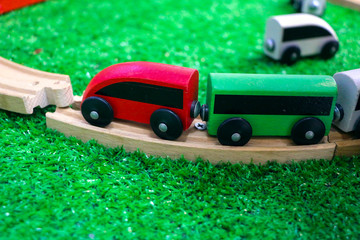 Children's wooden train with cars, railway and wooden trees on artificial plastic green grass. Early childhood education,  preschool and kids game concept.