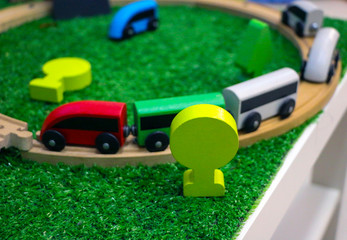 Children's wooden train with cars, railway and wooden trees on artificial plastic green grass. Early childhood education,  preschool and kids game concept.