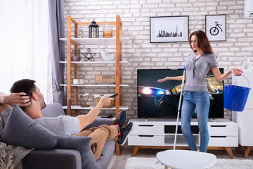 Woman Shrugging In Front Of Her Husband Watching Television