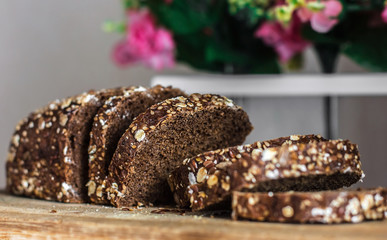 Rye bread with sliced ​​seeds. Sliced ​​black bread on the old wooden plank on the background of the decor of flowers
