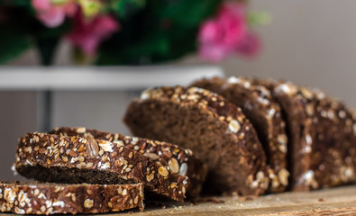Rye bread with sliced ​​seeds. Sliced ​​black bread on the old wooden plank on the background of the decor of flowers