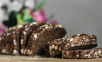Rye bread with sliced ​​seeds. Sliced ​​black bread on the old wooden plank on the background of the decor of flowers