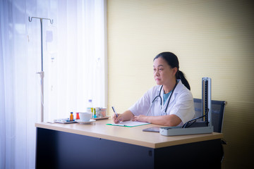 Obraz premium The closed up woman doctor with white uniform and medical devices such as stethoscope and blood pressure device is checking up the patient health and taking note on the white paper at the hospital