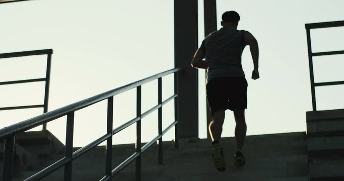 Back view of the Caucasian sporty guy jogging up the stairs at the stadium on a summer day. Rear. Outdoors.