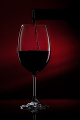 Red wine pouring in a glass from a bottle. Studio shot on black background.