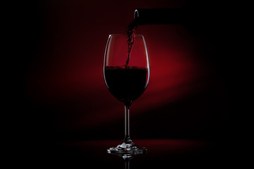 Pouring red wine from a bottle into a wine glass on a black background. Close-up studio shot.