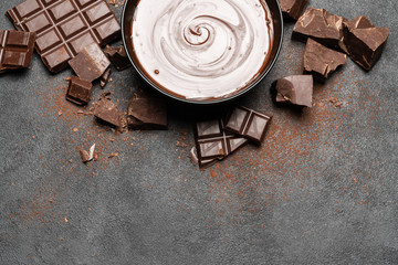 ceramic bowl of chocolate cream or melted chocolate and pieces of chocolate isolated on dark concrete background