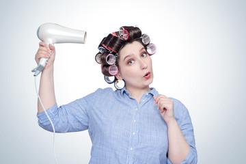 Young happy girl in a striped shirt with hair curlers on her head and a hairdryer