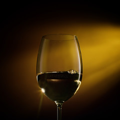 Naklejka na ściany i meble Glass of white wine on black to yellow background. Concept studio close-up shot.