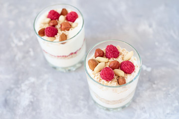 Two glasses of a greek yogurt granola with raspberries, oatmeal flakes and nuts, top view. Healthy nutrition